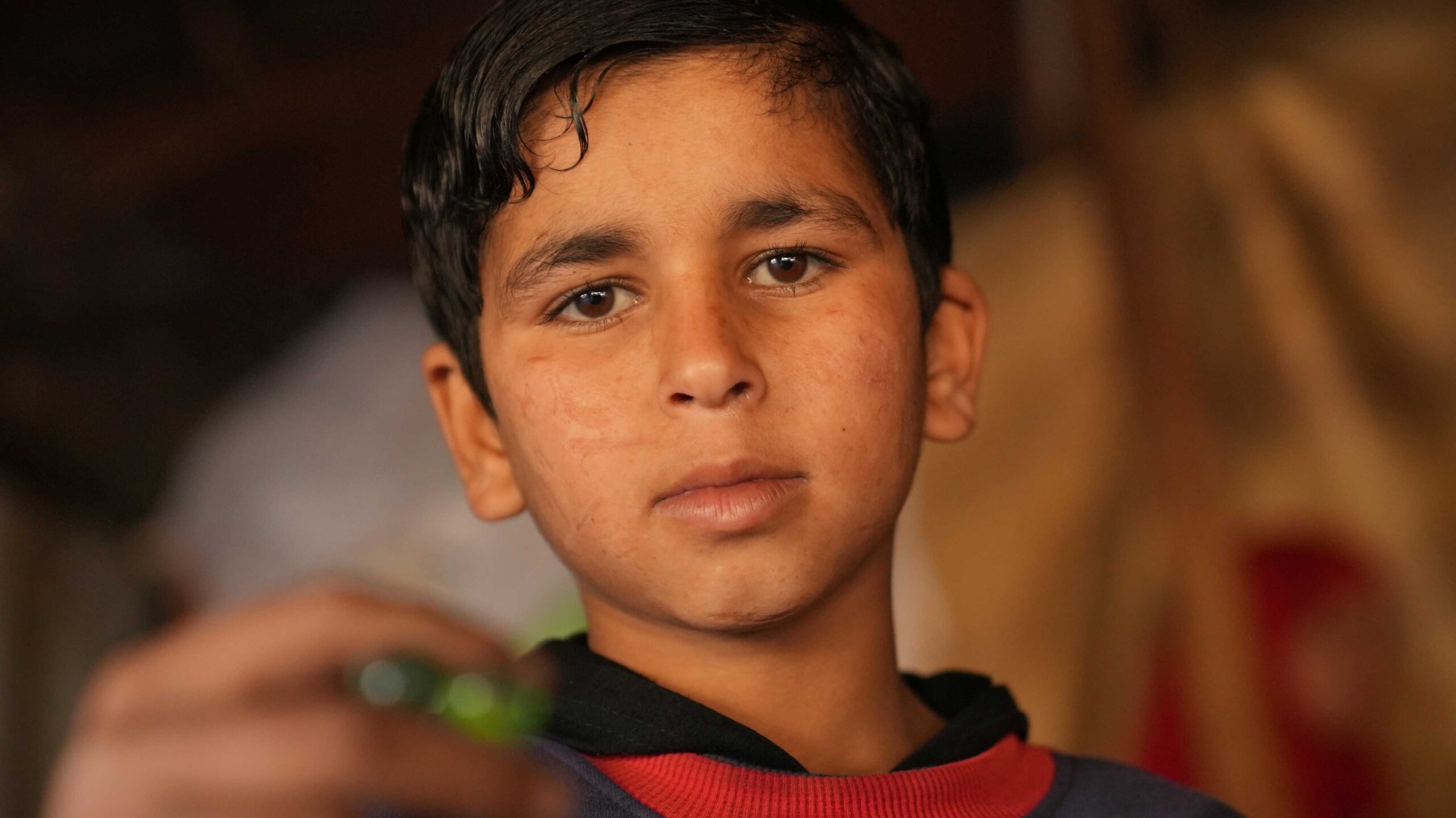 13 year old Azzam plays with marbles inside and outside his tent.