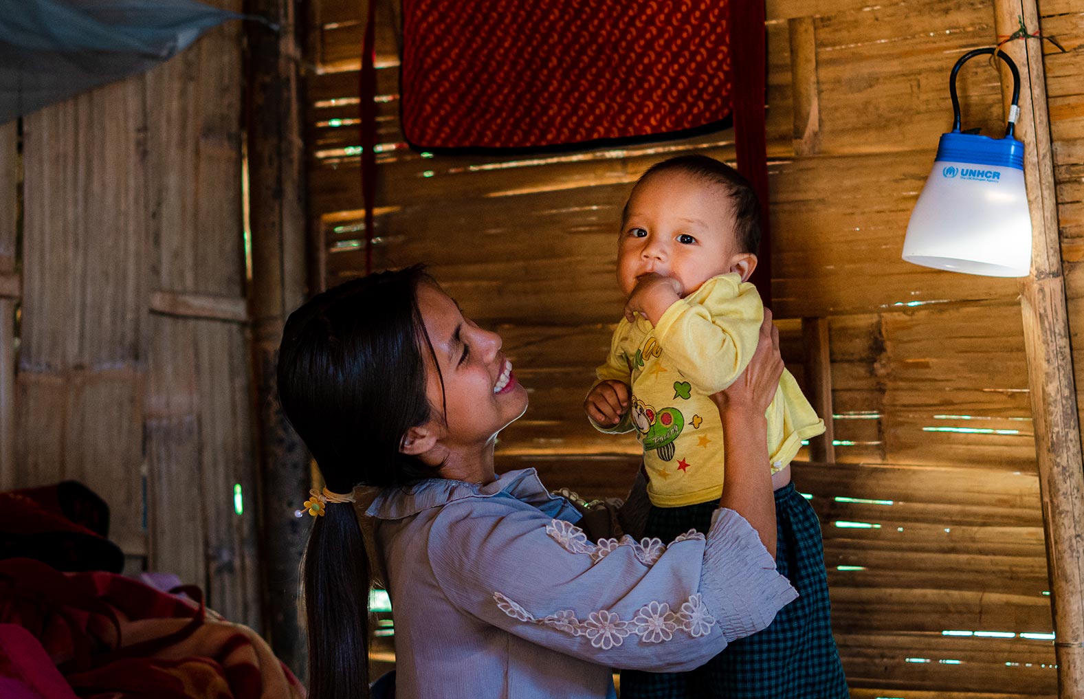 Si Mi Sar is playing with her child in a shelter which has been constructed for her family by UNHCR and its partners in a village in Kachin State.